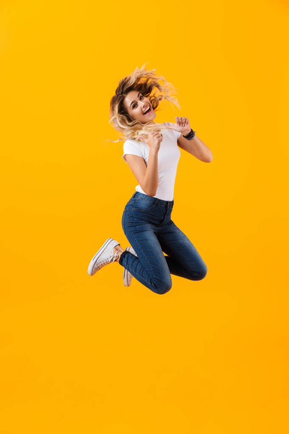 Full length photo of european blond woman in basic clothing jumping and laughing isolated over yellow background - Foto, Imagem
