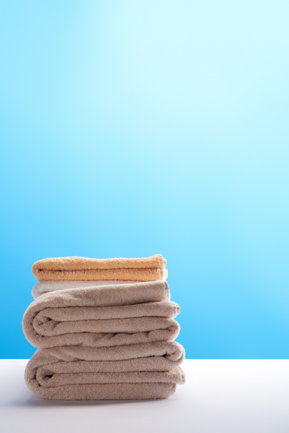 stack of clean fresh towels on white table on blue background   - Φωτογραφία, εικόνα