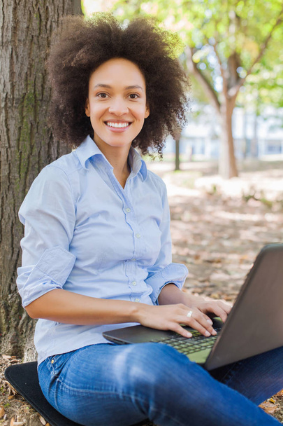  Doğada boş bir gün, güzel, mutlu bir Afrikalı kadın öğrencinin dizüstü bilgisayarla çalışması, parkta oturması, açık hava portresi giymesi, , - Fotoğraf, Görsel
