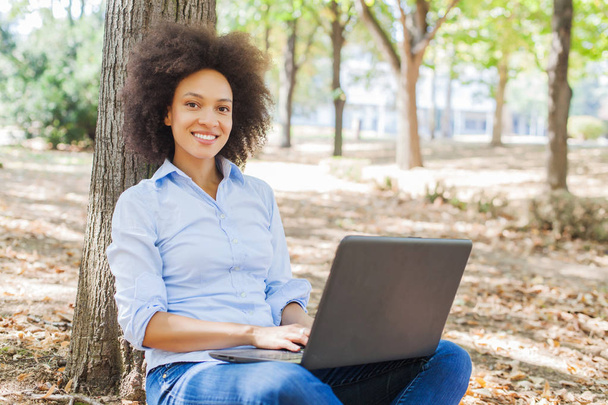  Día libre en la naturaleza, Hermosa mujer africana feliz estudiante que trabaja con el ordenador portátil, Sentado en el suelo en el parque, Retrato al aire libre, Lleva ropa casual
 , - Foto, Imagen