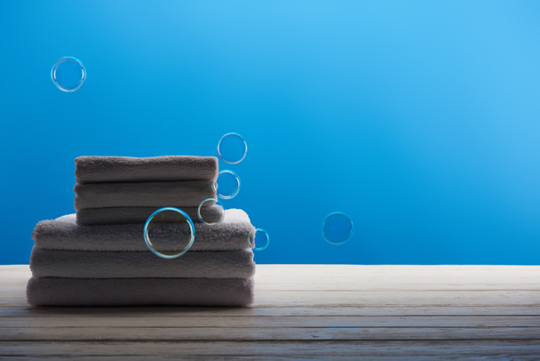 schone witte handdoeken en zeepbellen op blauwe achtergrond     - Foto, afbeelding