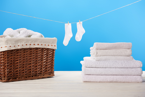 laundry basket, pile of clean soft towels and white socks hanging on rope on blue  - Zdjęcie, obraz