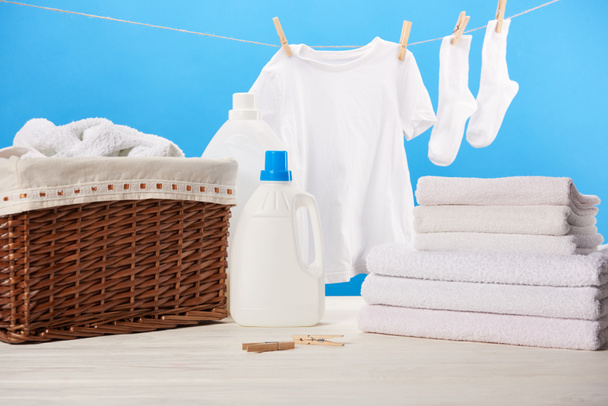 Plastikbehälter mit Waschflüssigkeiten, Wäschekorb, Handtüchern und sauberer weißer Kleidung auf blauem Grund  - Foto, Bild