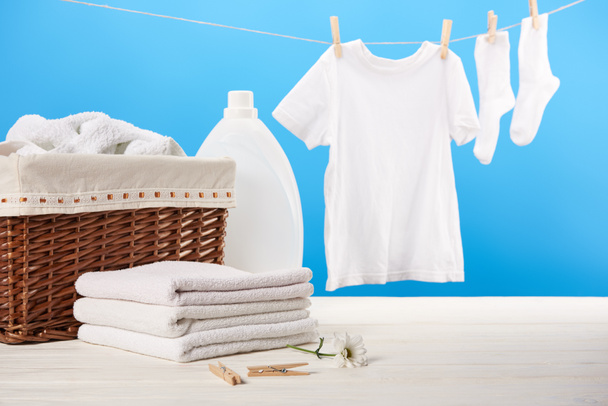 cesta de la ropa, recipiente de plástico con líquido de lavandería, pila de toallas suaves limpias y ropa blanca colgando en el tendedero en azul
   - Foto, Imagen