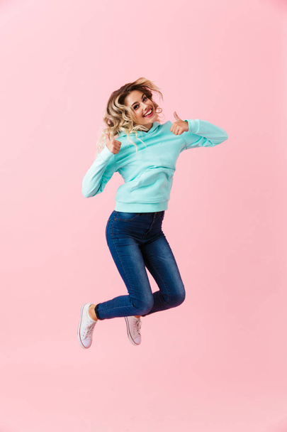 Full length image of beautiful woman in basic clothing jumping and showing thumbs up isolated over pink background - Fotoğraf, Görsel
