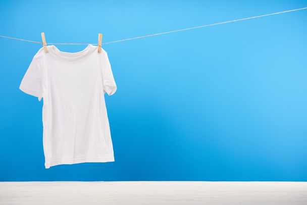 clean white t-shirt hanging on rope on blue  - Zdjęcie, obraz