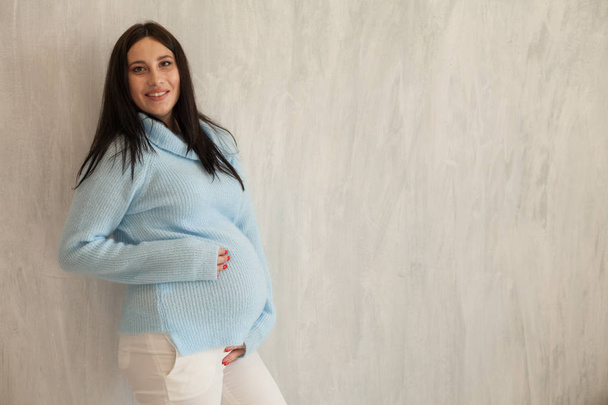 Porträt einer schwangeren Frau im blauen Kleid graue Wände - Foto, Bild