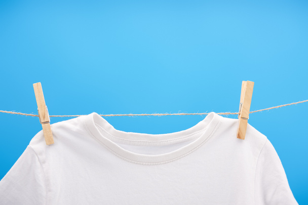 vue rapprochée du t-shirt blanc propre avec des pinces à linge suspendues à une corde isolée sur bleu
   - Photo, image