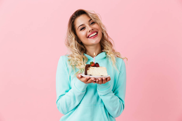 Photo of happy woman in basic clothing holding piece of birthday cake with candle isolated over pink background - Foto, Bild