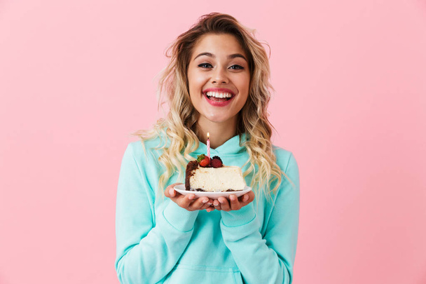 Photo of gorgeous woman in basic clothing holding piece of birthday cake with candle isolated over pink background - Photo, image