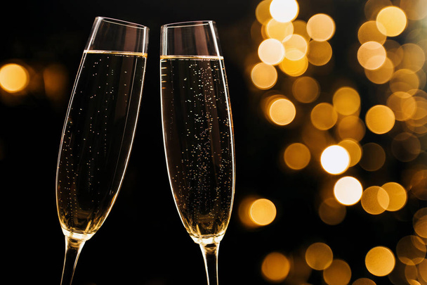 Two glasses of champagne on black stylish background with golden bokeh circles. Place for text. Festive concept. - Fotó, kép