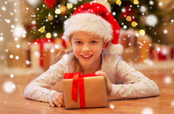 smiling girl in santa hat with christmas gift - 写真・画像