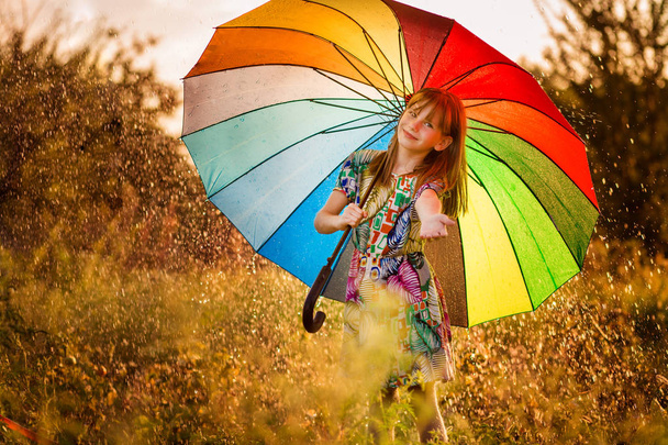 Ευτυχισμένο παιδί κορίτσι με τα πόδια με πολύχρωμη ομπρέλα κάτω από φθινοπωρινή βροχή  - Φωτογραφία, εικόνα