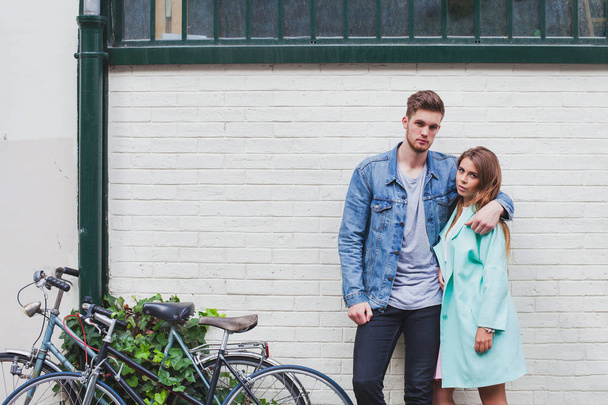 portrait of young beautiful fashion caucasian couple looking at camera on the street, stylish man and woman with bicycles - Fotó, kép