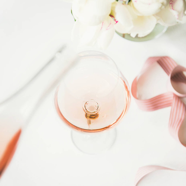 Vinho rosa em vidro e garrafa, fita decorativa rosa e flores de peônia sobre fundo branco, espaço de cópia, colheita quadrada. Celebração de verão, cartão de felicitações de casamento ou conceito de convite
 - Foto, Imagem