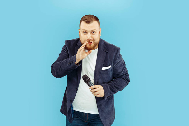 Young man with microphone on blue background, leading concept - Foto, afbeelding