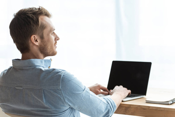vue arrière du jeune homme d'affaires travaillant sur un ordinateur portable avec écran blanc à la table dans le bureau
  - Photo, image