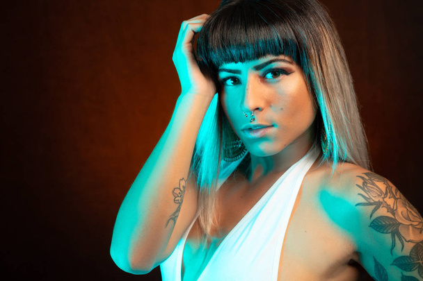 Alternative model with bangs and colored hair poses under blue light wearing a white leotard - Foto, afbeelding