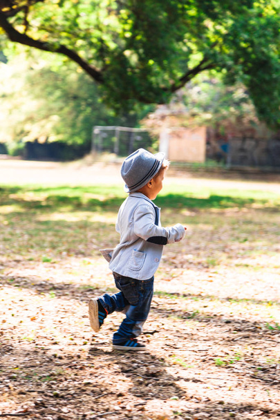 Cute little boy in hat running outdoors in sunny day - Photo, image