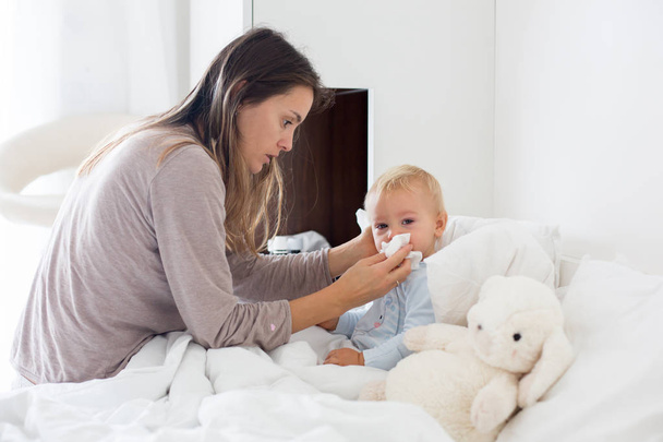 Mother and baby in pajamas, early in the morning, mom taking care of her sick toddler boy. Baby in bed with fever and running nose - Фото, зображення