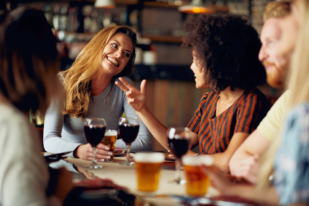 Přátelé, chatování a pití alkoholu při posezení v restauraci. Etnická skupina multi. - Fotografie, Obrázek