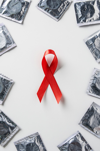 Draufsicht auf Hilfsmittel Bewusstsein rotes Band und silberne Kondome auf weißem Hintergrund - Foto, Bild