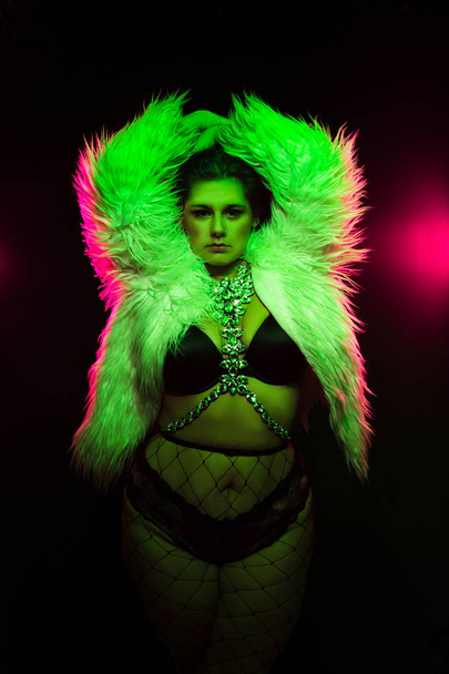 Curvy alternative model with colored hair and fur coat and fishnets under green and pink lighting - Фото, изображение