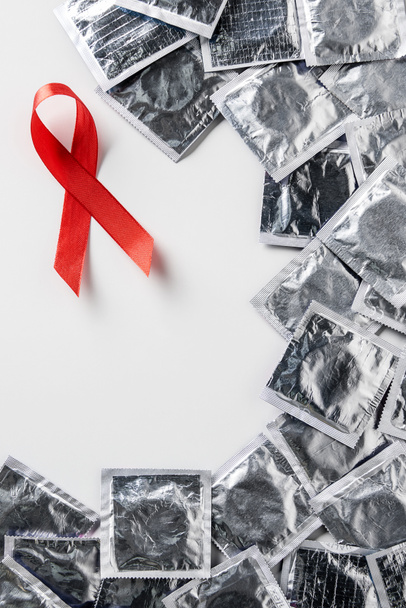 top view of aids awareness red ribbon and silver condoms on white background - Foto, Bild