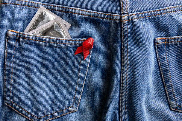 Aids awareness red ribbon and silver condoms in pocket of blue jeans
 - Фото, изображение