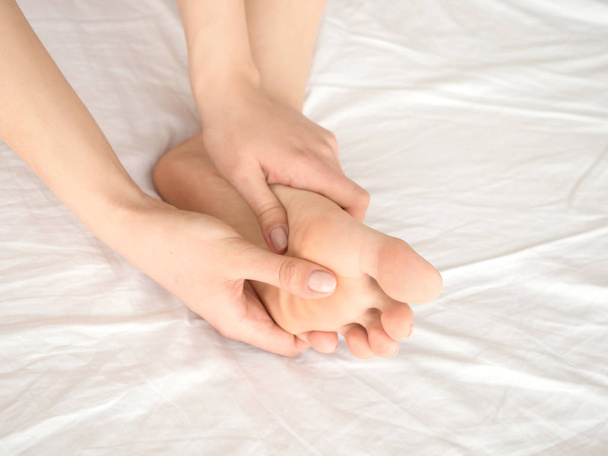 Stóp ból nogi kobieta siedziała na łóżku w w domu i fassaging jej stopy. Opieki zdrowotnej i koncepcja spa - Zdjęcie, obraz
