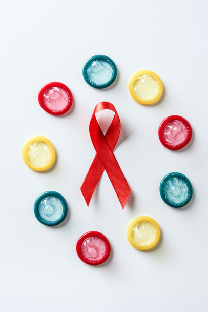 top view of aids awareness red ribbon and multicolored condoms on white background - Zdjęcie, obraz