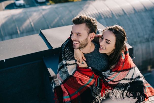 high angle view of laughing young couple covered in plaid sitting on rooftop together - Fotografie, Obrázek