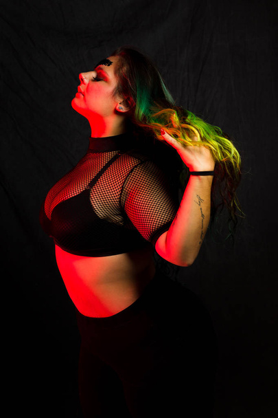 Curvy alternative model with colored hair and mesh clothing poses under red lighting - Valokuva, kuva