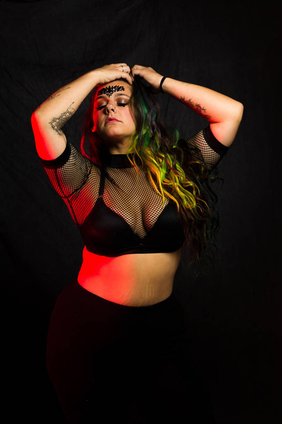 Curvy alternative model with colored hair and mesh clothing poses under red lighting - Fotoğraf, Görsel