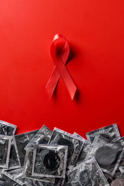 top view of aids awareness red ribbon and silver condoms on red background - Foto, imagen
