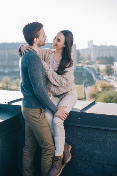 smiling young couple embracing and looking at each other on rooftop - Fotografie, Obrázek