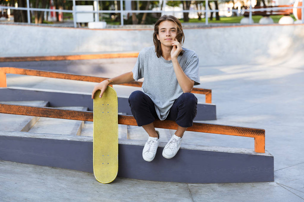 Image of handsome young skater guy sit in the park with skateboard. - Foto, Bild