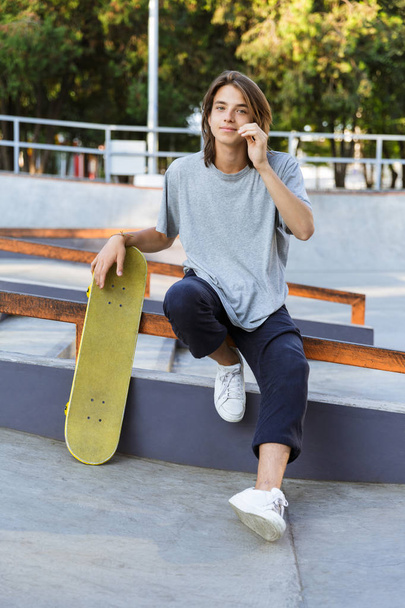 Image of handsome young skater guy sit in the park with skateboard. - Φωτογραφία, εικόνα