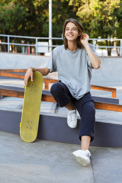 Image of handsome young skater guy sit in the park with skateboard. - Photo, image