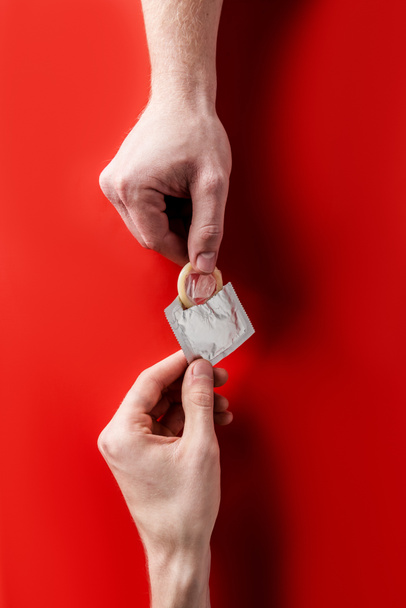 Widok z góry ręce trzymając prezerwatywę na czerwonym tle - Zdjęcie, obraz