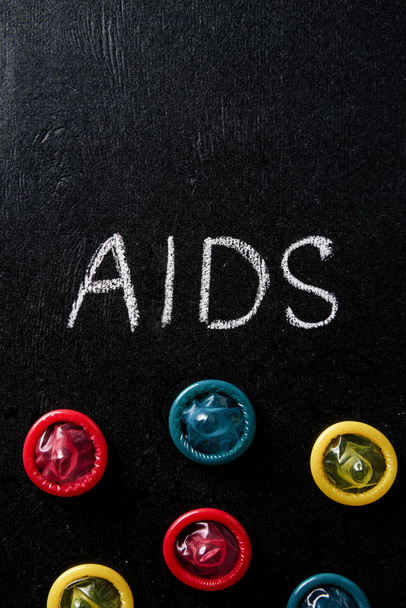 κάτοψη του aids πινακίδα με πολύχρωμα προφυλακτικά σε μαύρο φόντο - Φωτογραφία, εικόνα