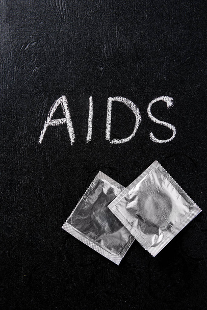 vista superior del signo de sida y condones plateados sobre fondo negro
 - Foto, Imagen