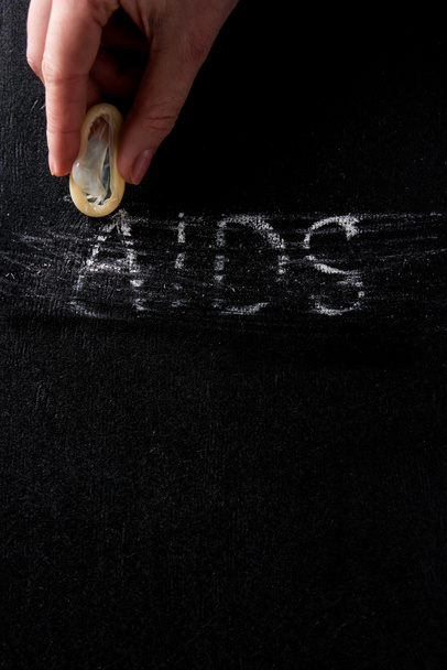 top view female hand holding condom with aids sign on black background - Foto, imagen
