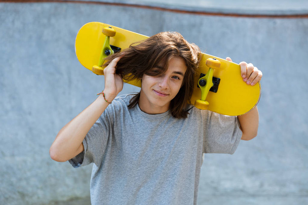 Happy young teenge boy spending time at the skate park, holding a skateboard - Fotoğraf, Görsel