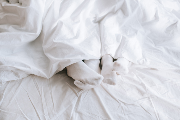 rajattu laukaus pari valkoisissa sukissa rentouttava sängyssä peiton alla
 - Valokuva, kuva