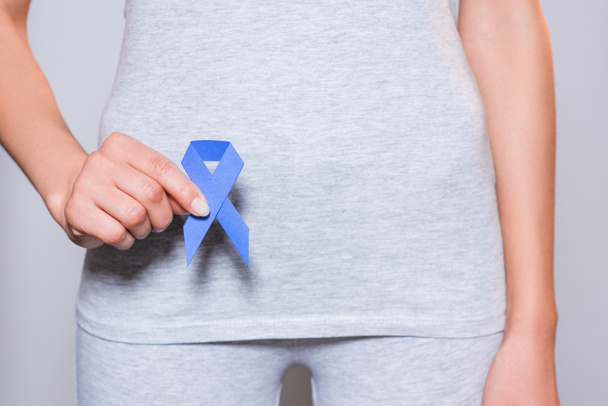 partial view of woman holding prostate cancer awareness blue ribbon in hand on grey backdrop - Fotografie, Obrázek