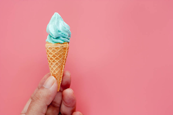 Hand holding ice cream cone on pink background for sweet and refreshing dessert concept - Фото, изображение