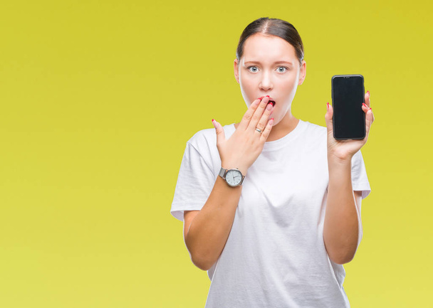 Młodych piękne kaukaski kobieta pokazując ekran smartfona na na białym tle okładka usta ręką w szoku ze wstydem za błąd, wyrażenie strachu, przestraszony w milczeniu, tajne koncepcja - Zdjęcie, obraz
