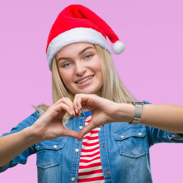 Young caucasian woman wearing christmas hat over isolated background smiling in love showing heart symbol and shape with hands. Romantic concept. - Foto, imagen