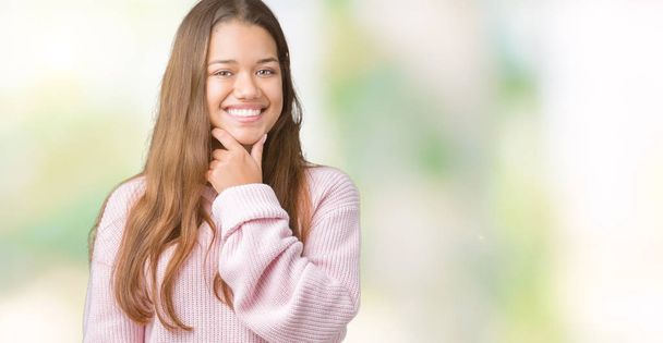 Mladá krásná bruneta žena nosí růžové zimní svetr přes samostatný pozadí sebevědomým na kameru s úsměvem se zkříženýma rukama a ruku a na bradě. Pozitivní myšlení. - Fotografie, Obrázek